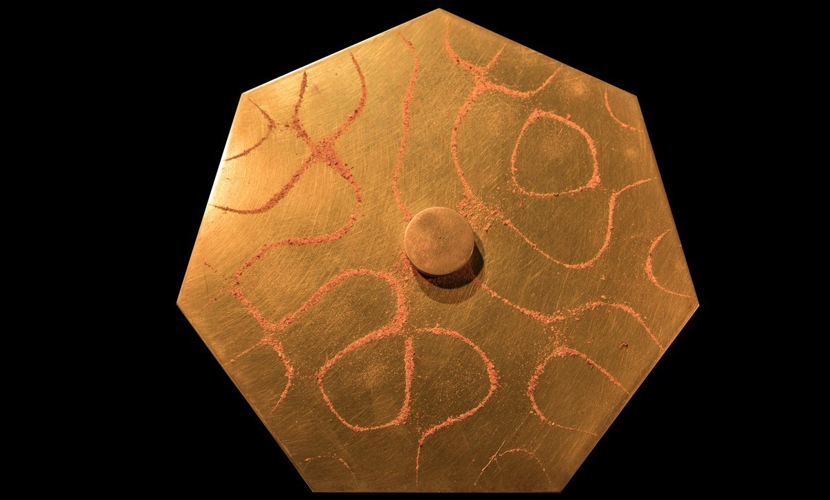 Chladni figure on a heptagonal brass plate showing complex nodal line patterns in red sand