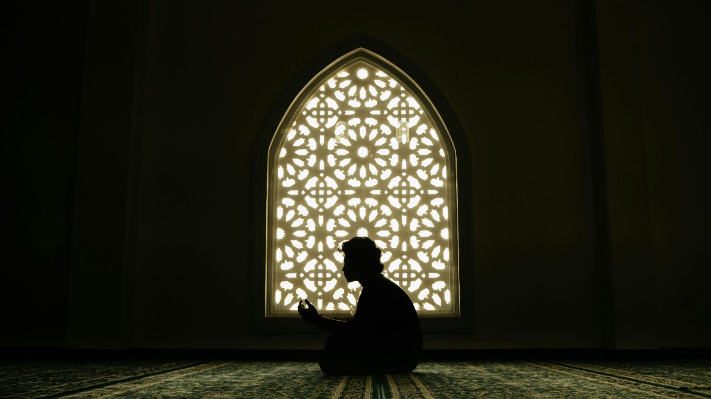Silhouette of a worshipper before an illuminated geometric window in a mosque